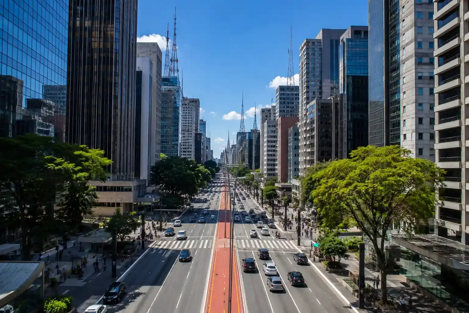 Avenida Paulista vista do alto, com arranha-céus, ciclovia vermelha e árvores sob céu azul em São Paulo
