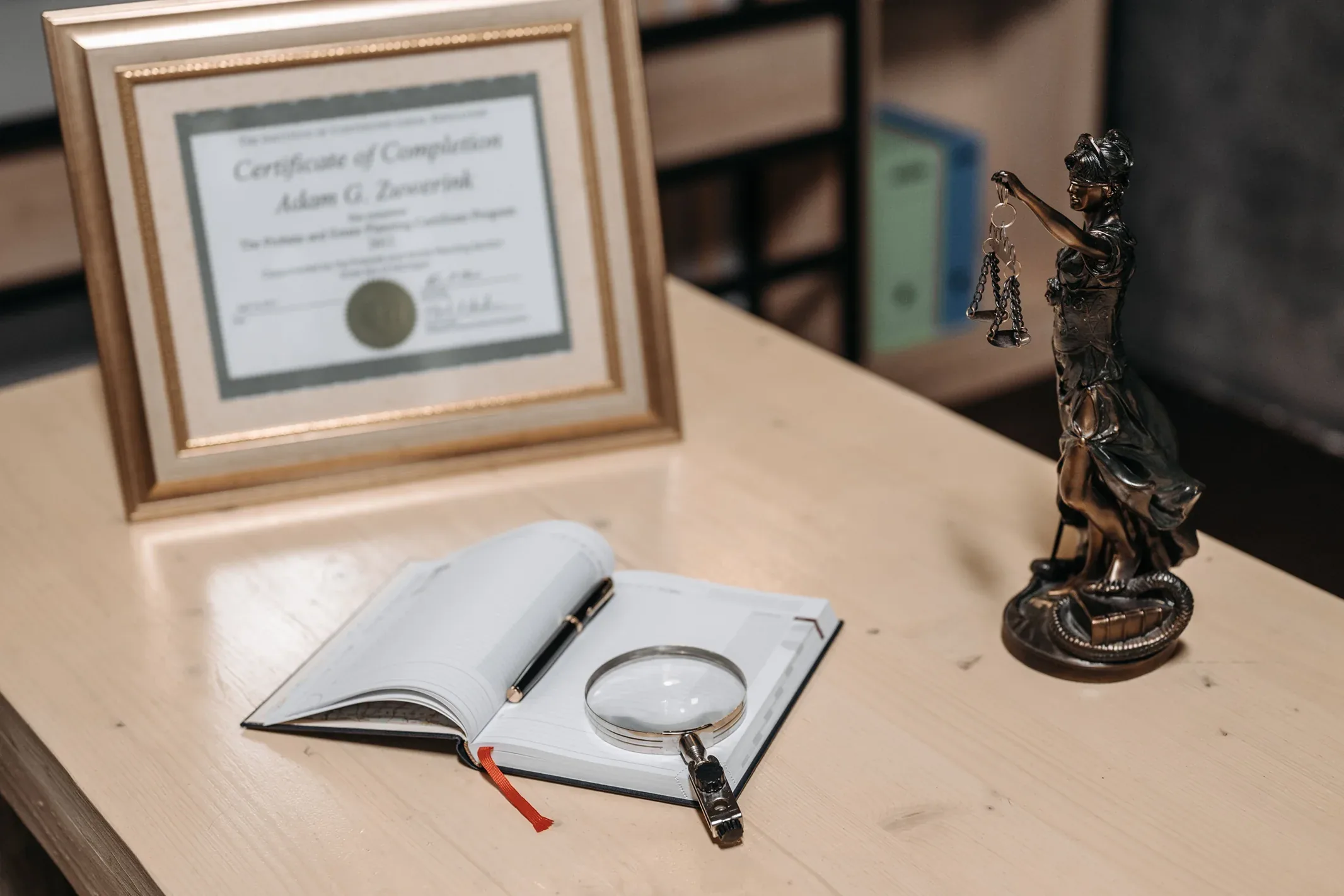 Mesa com diploma emoldurado, caderno com lupa e estatueta da Justiça, ilustrando tradução juramentada de alemão