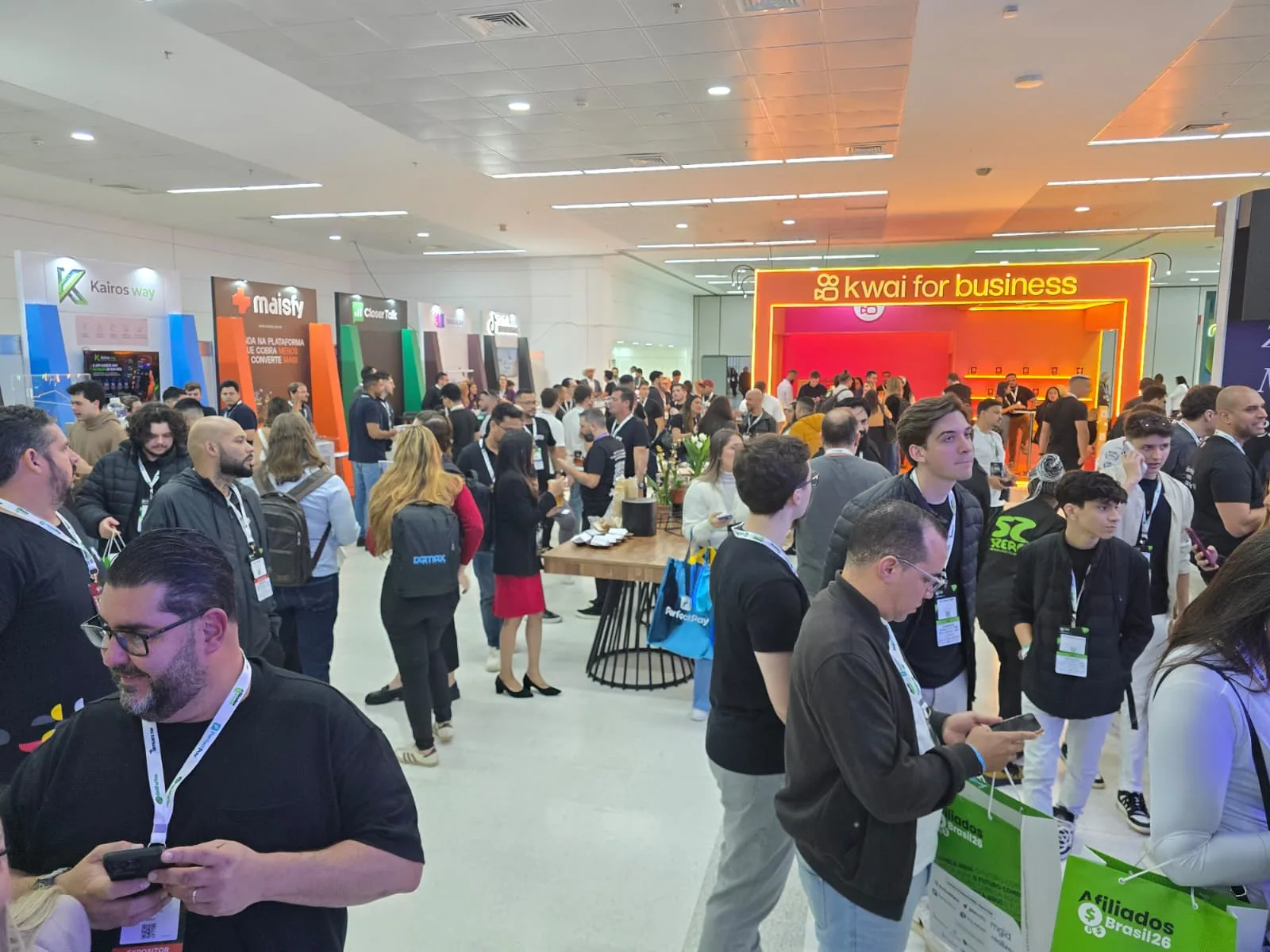 Visitors with badges at an affiliate marketing event in São Paulo, company booths in the background