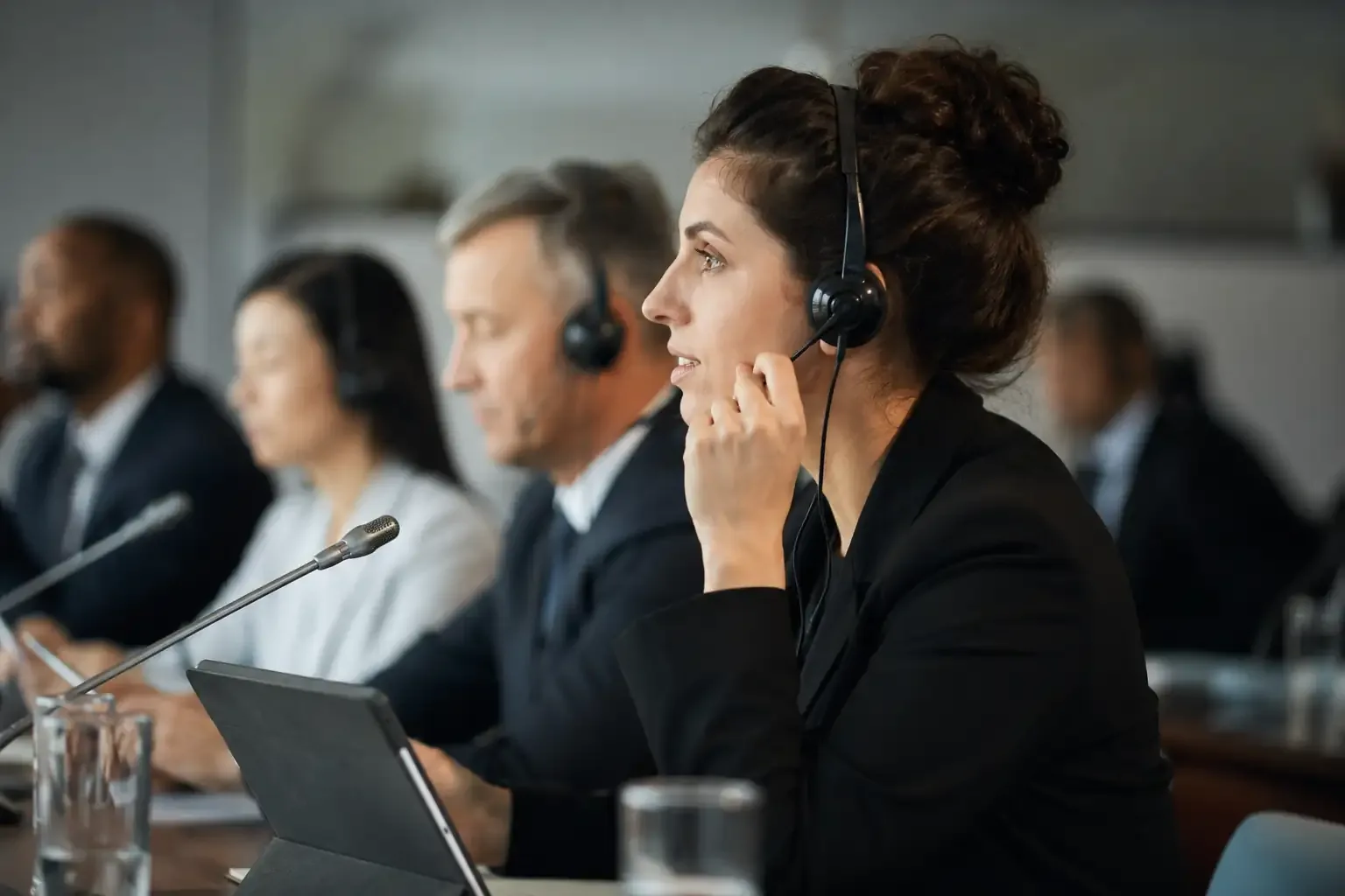 Intérprete de fone atenta ao lado de participantes também de fone em reunião de negócios com microfones de mesa